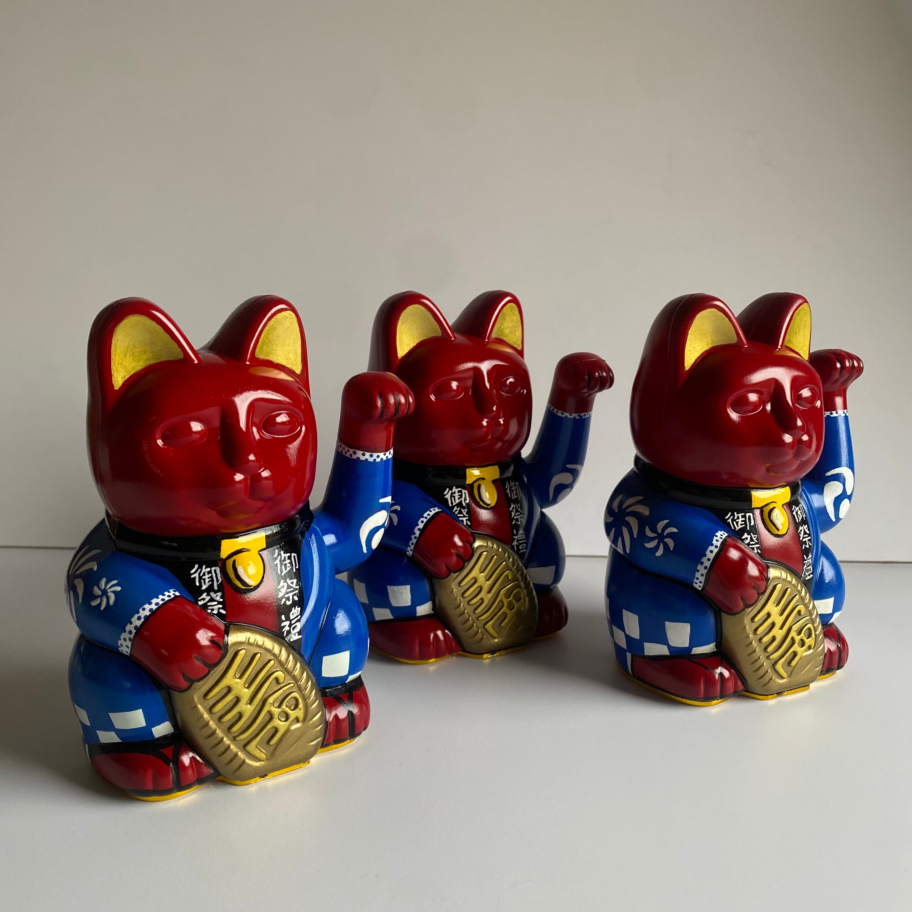 Three red cat-shaped figurines with blue outfits on a light gray background