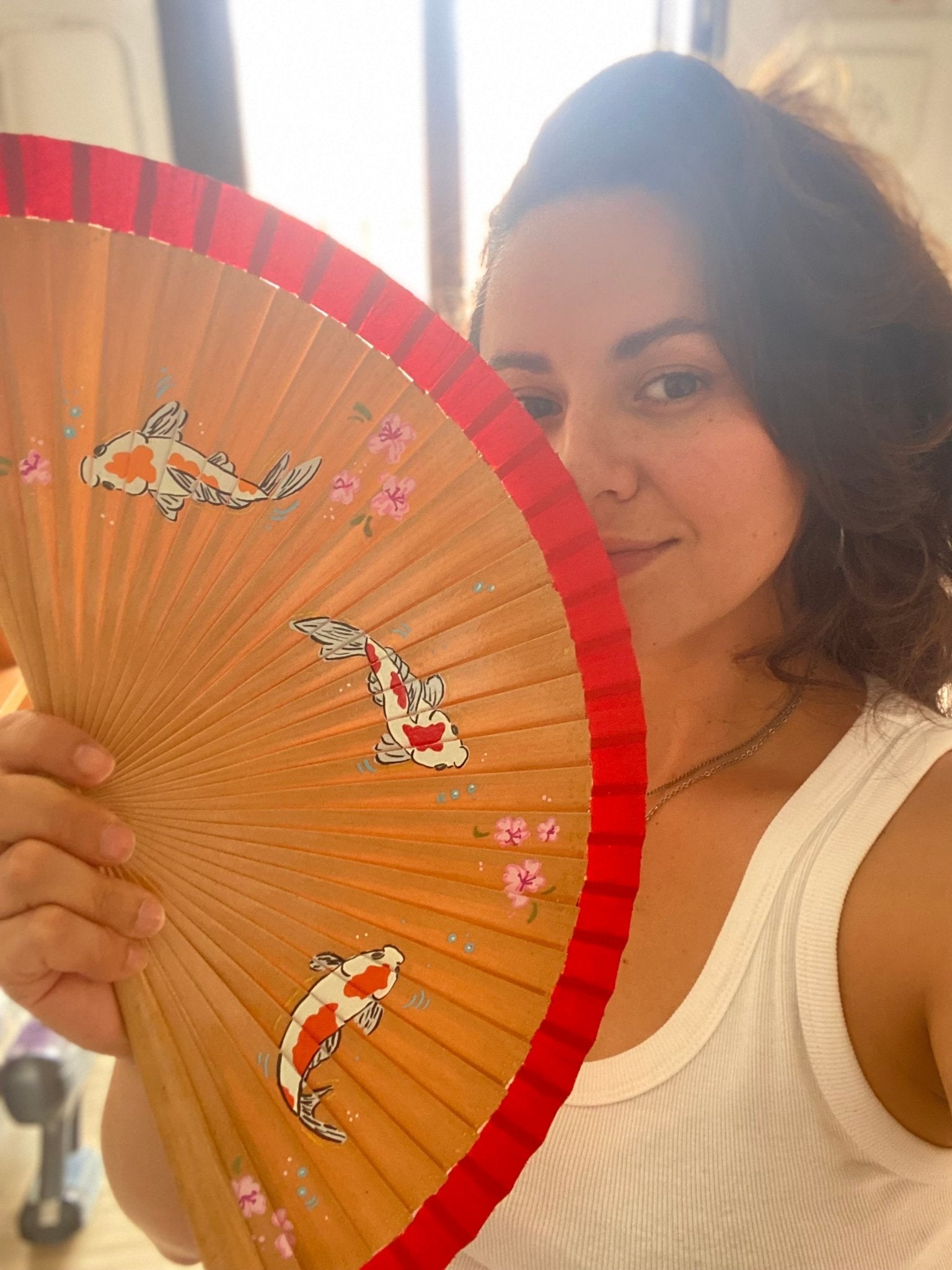 Woman holding a decorative fan with koi fish designs.