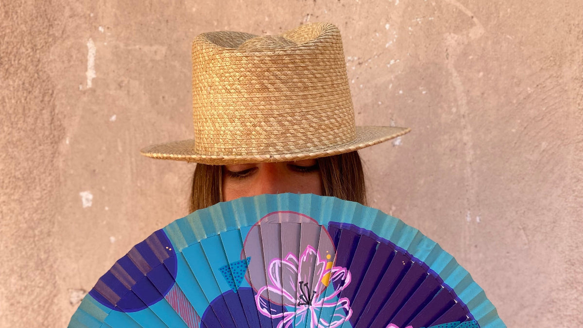 Person holding a decorative fan with floral designs against a textured wall.